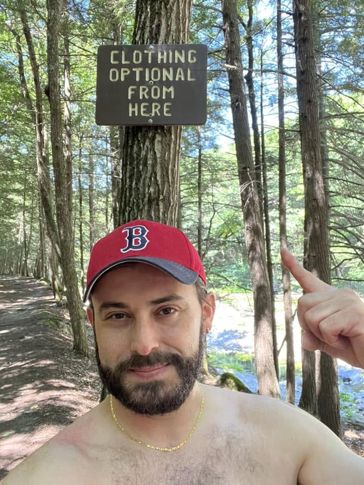 The clothing-optional sign Visitor pointing to the hand-lettered “Clothing optional from here” sign on a hemlock beside the Rock River trail in Newfane, Vermont